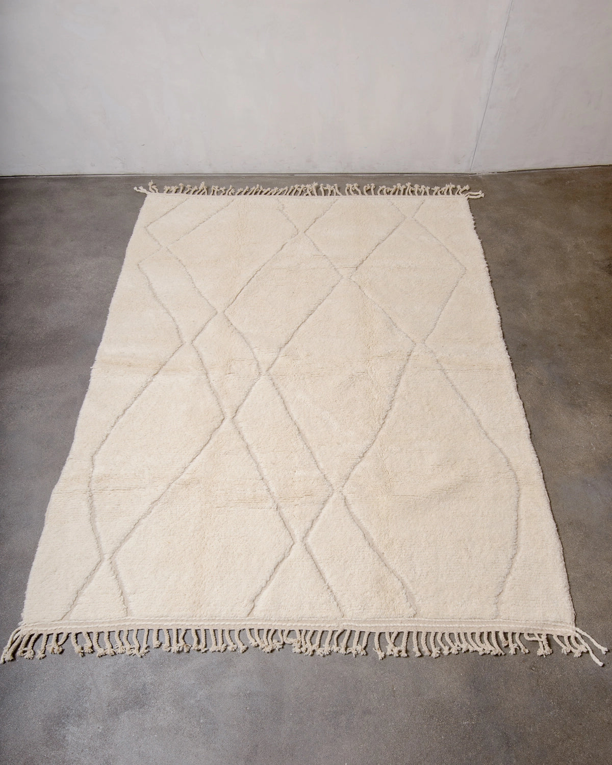 Berberlin Beniourain Rug made of natural cream wool with an abstract woven diamond design, photographed flat on concrete floor.